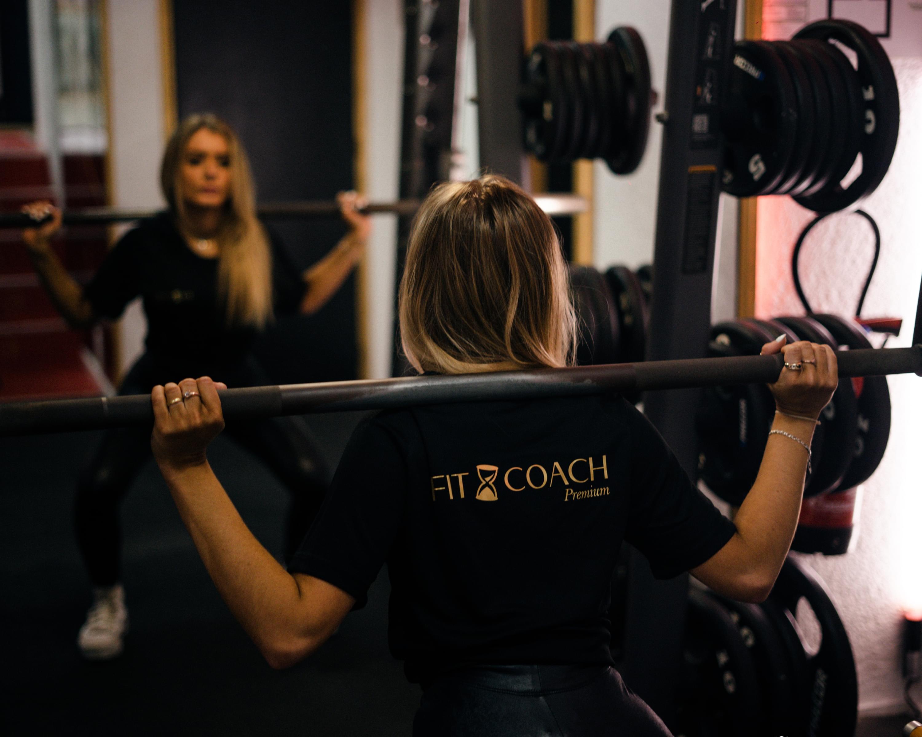 Fit girl avec un T-Shirt Fit And Coach en train de faire un squat avec une barre sur les épaule